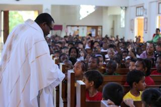 Fr. Tullock, SJ, greets children at St. Anne's Church. Source: inourcompany.org